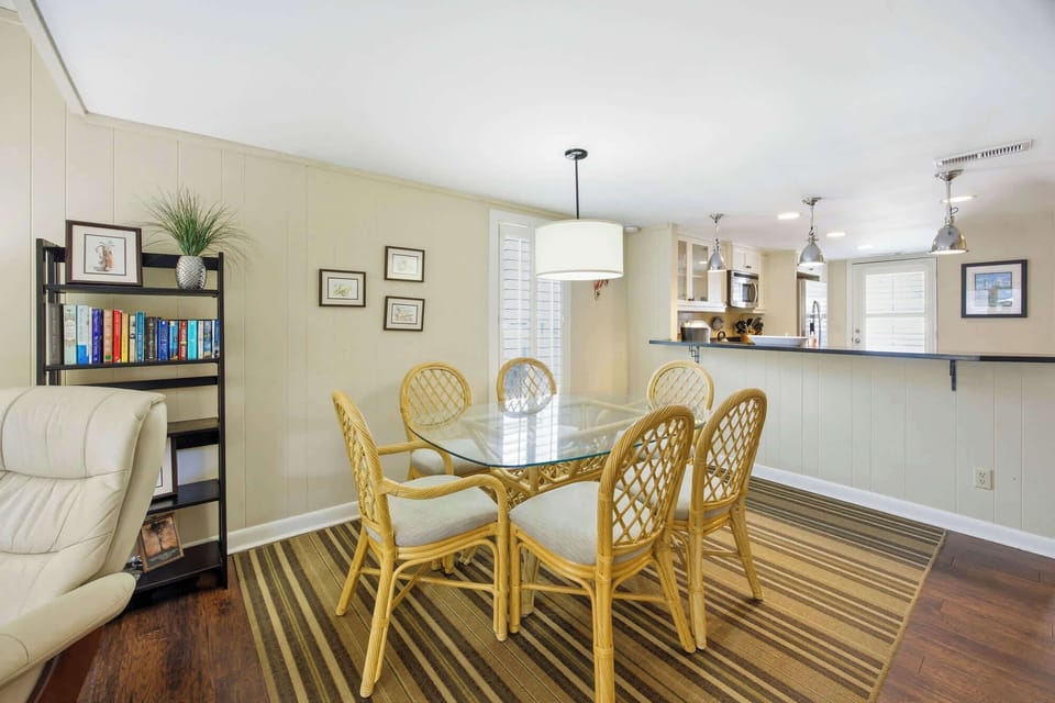 Dining area with rattan chairs and a glass table adjacent to a modern kitchen bar.