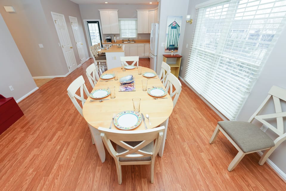 12 Dune Road - Tower Shores - Dining Area - A welcoming dining area with a light wood table, coastal white chairs, and warm wood flooring.