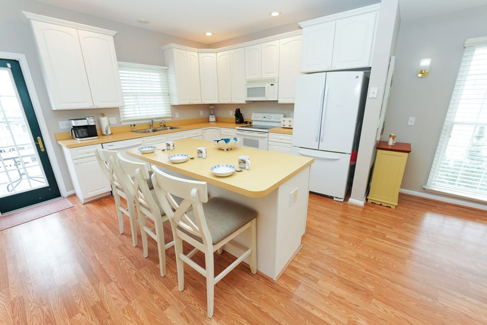 12 Dune Road - Tower Shores - Full Kitchen View - A full perspective of the bright white kitchen cabinetry, modern appliances, and convenient access to the outdoor deck.