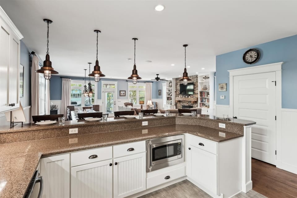 221 Wellington Parkway Kitchen Island with Breakfast Bar and Pen - A view of the large kitchen island featuring a breakfast bar with place settings, dark countertops, and stylish black pendant lights overhead.