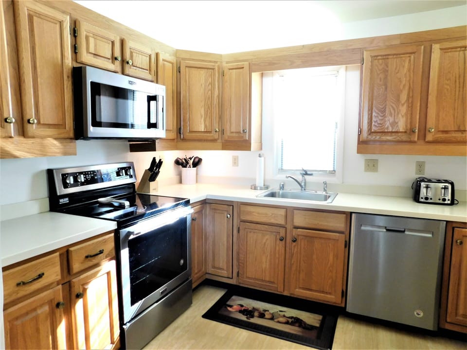 324 Seabreeze, The Canal - Kitchen Cooking Workspace - Functional cooking area at 324 Seabreeze, The Canal, featuring an electric range, over-the-range microwave, and ample oak cabinet storage for vacation meal prep.