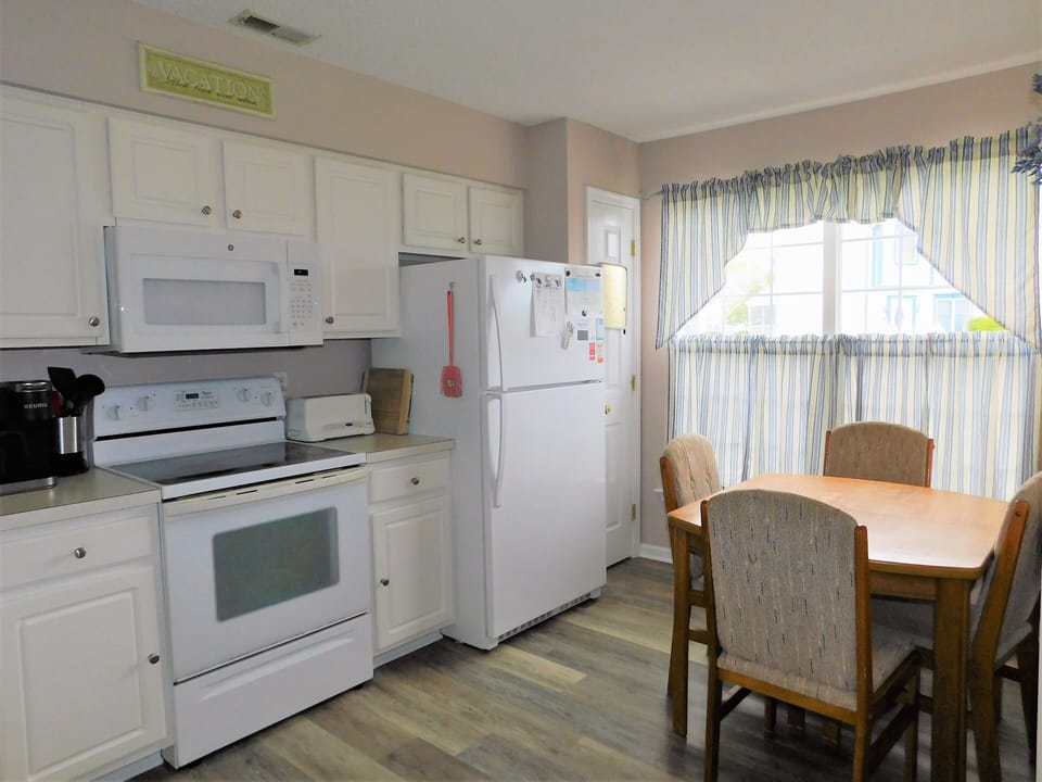 33 Thistle Lane - Kitchen & Nook Overview - Perspective of the kitchen area highlighting the electric range, built-in microwave, and the adjacent sun-drenched breakfast table.