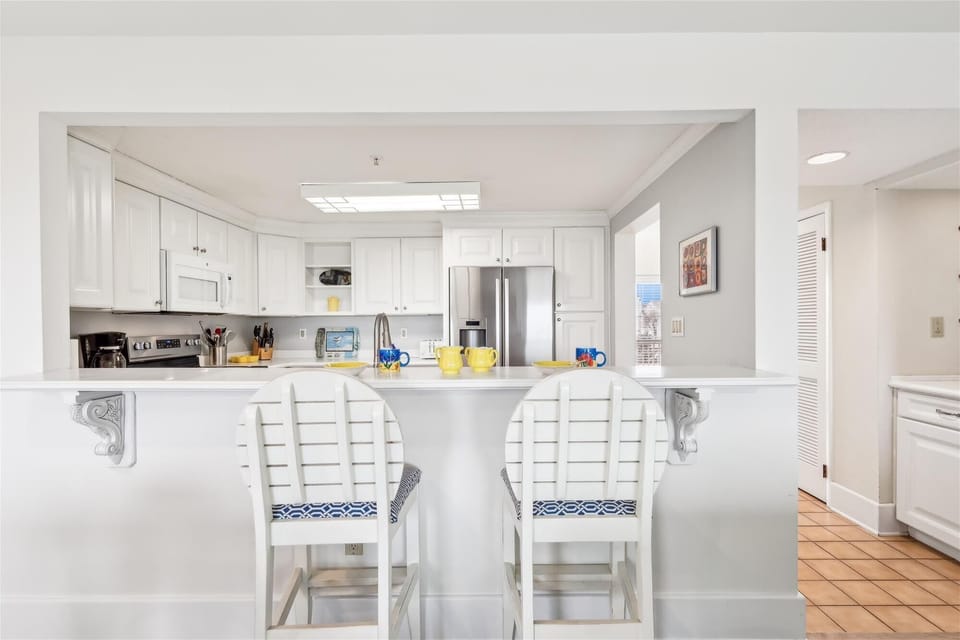 35 Kings Grant, Fenwick Island - Breakfast Bar - View of the kitchen pass-through featuring a white counter with two white wooden stools.
