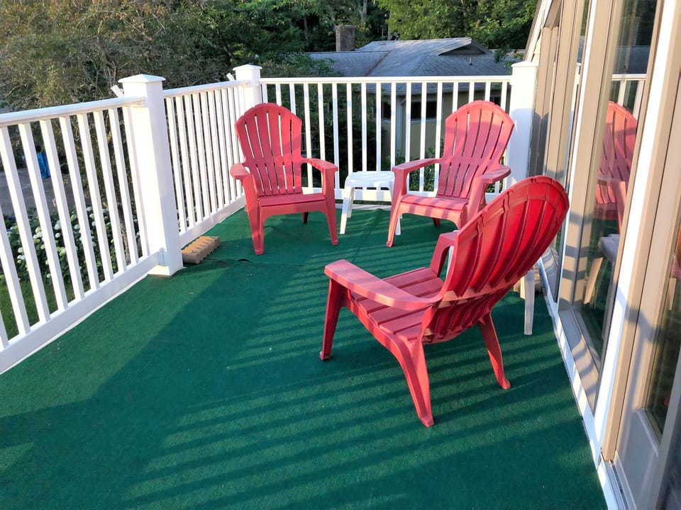 612 Paget Court - Spacious Outdoor Observation Deck - The home features an expansive upper-level deck with green outdoor carpeting and vibrant red Adirondack chairs. Surrounded by a white railing, this elevated space offers a perfect vantage point for enjoying the wooded neighborhood views.