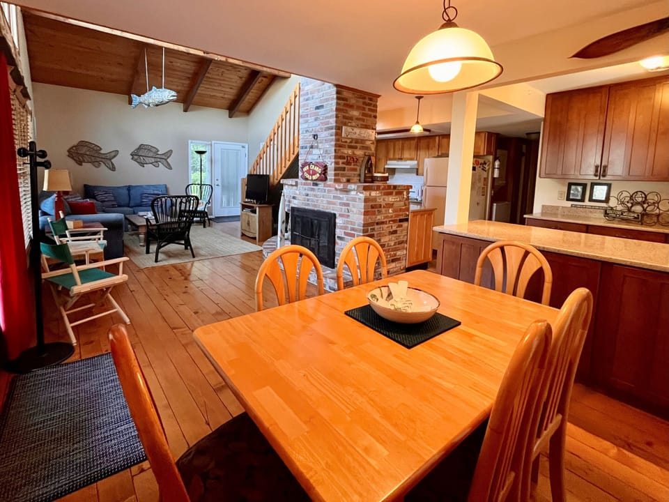 Bright Dining and Living Integration - This perspective showcases the seamless flow from the dining table into the sun-drenched living area, emphasizing the home's suitability for group gatherings. Vaulted ceilings and warm wood tones continue throughout the main level.
