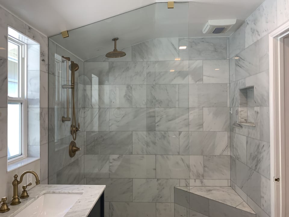 Floor to ceiling marble master bath shower with a bench seat and handheld shower
