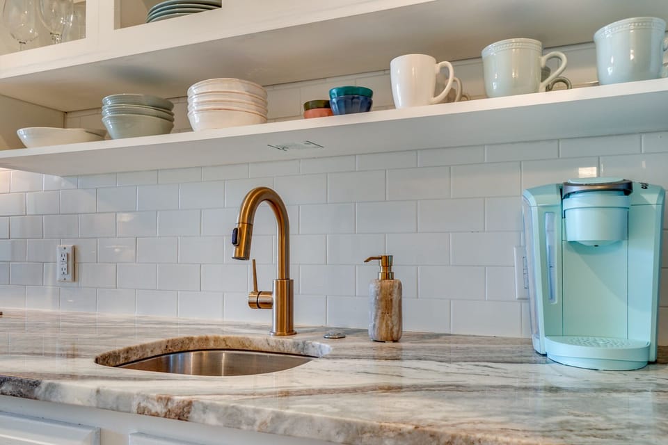 Your morning coffee ritual awaits in this elegant kitchen with gleaming marble countertops, brass fixtures, and everything perfectly arranged for your culinary adventures.