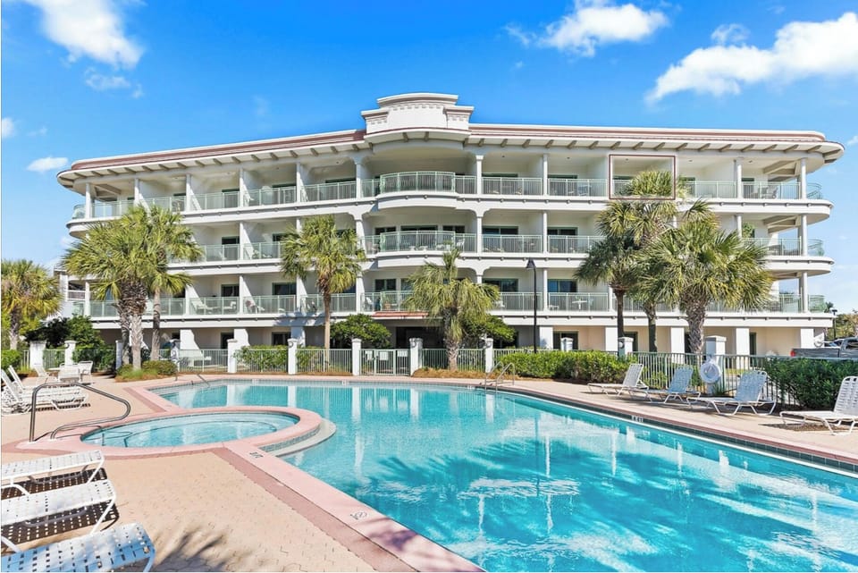 Modern beachside resort with sparkling pool area and tropical landscaping under clear blue skies.
