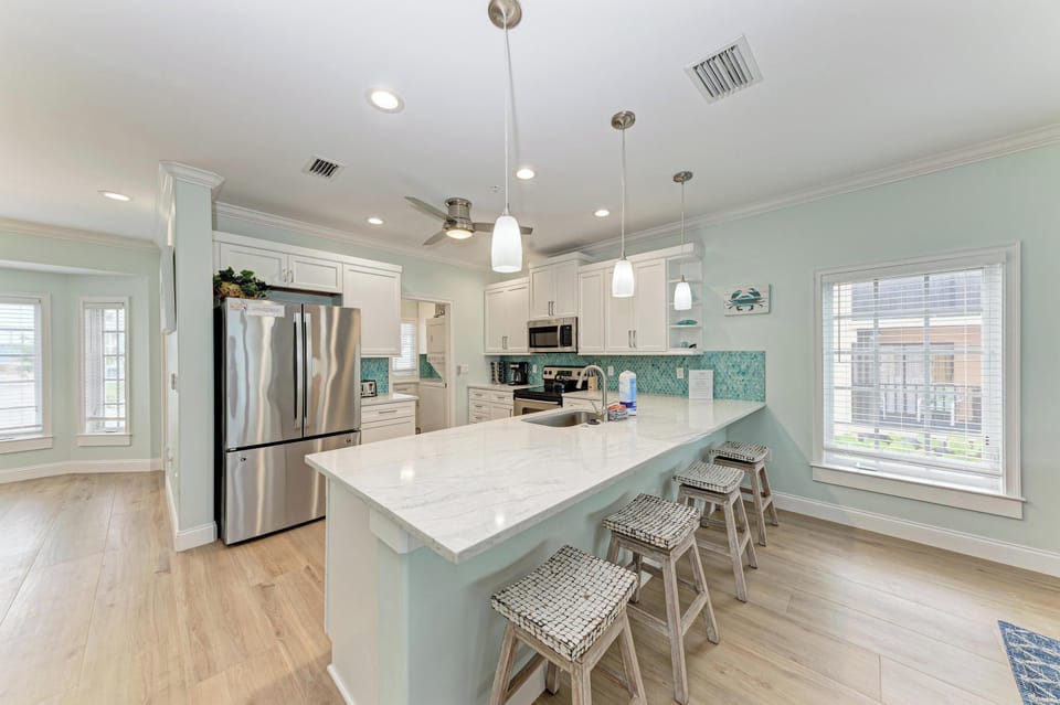 Gather around this bright, coastal-inspired kitchen where your meals take center stage. The spacious island invites conversation while soft aqua tones and marble counters create a refreshing, beachy vibe.