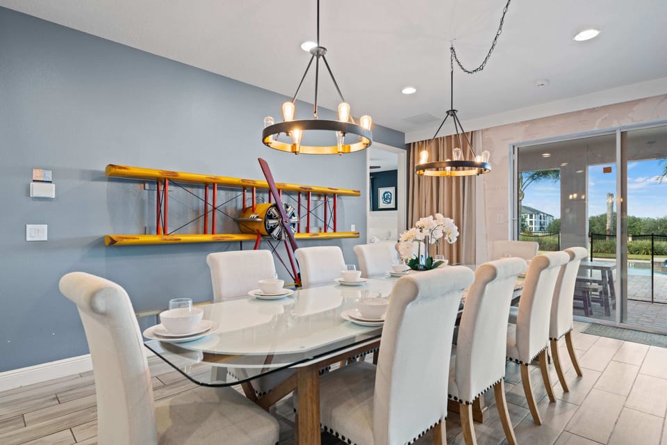 - Dining room with airplane propeller wall decor as centerpiece  
- Long glass table with seating for group meals and celebrations  
- Bright space with lighting and pool views through glass doors
