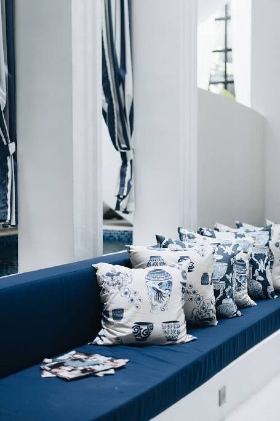 A nook of comfort: blue bench, patterned pillows, blue & white curtains.