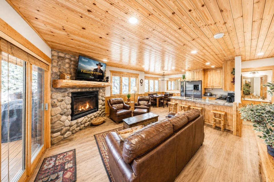 Gather around the warm stone fireplace and sink into rich leather seating. This open-concept space blends rustic wood charm with modern comfort—your perfect mountain retreat.