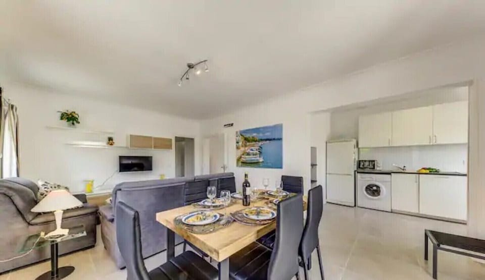Dining table for six next to the lounge and an open-plan kitchen with fridge, washer and microwave.