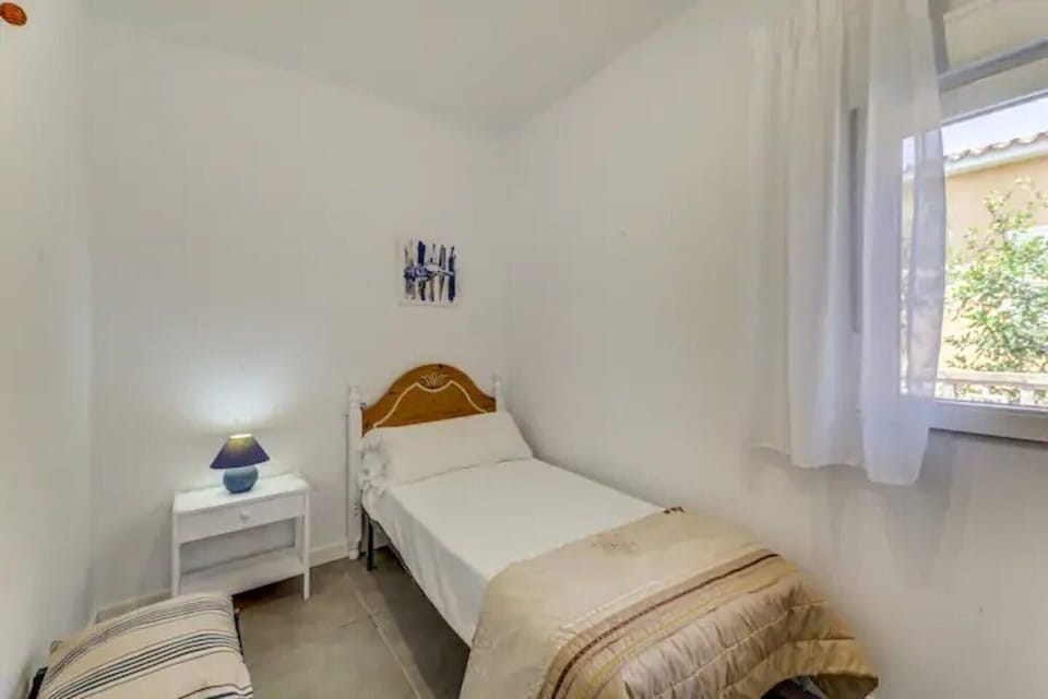 Single bedroom with bed, blue bedside lamp, exterior window and simple décor.