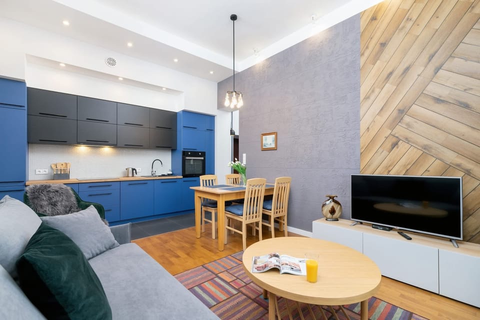 A combined living and dining space with a gray sofa, a wooden dining table, and a television mounted on the wall.