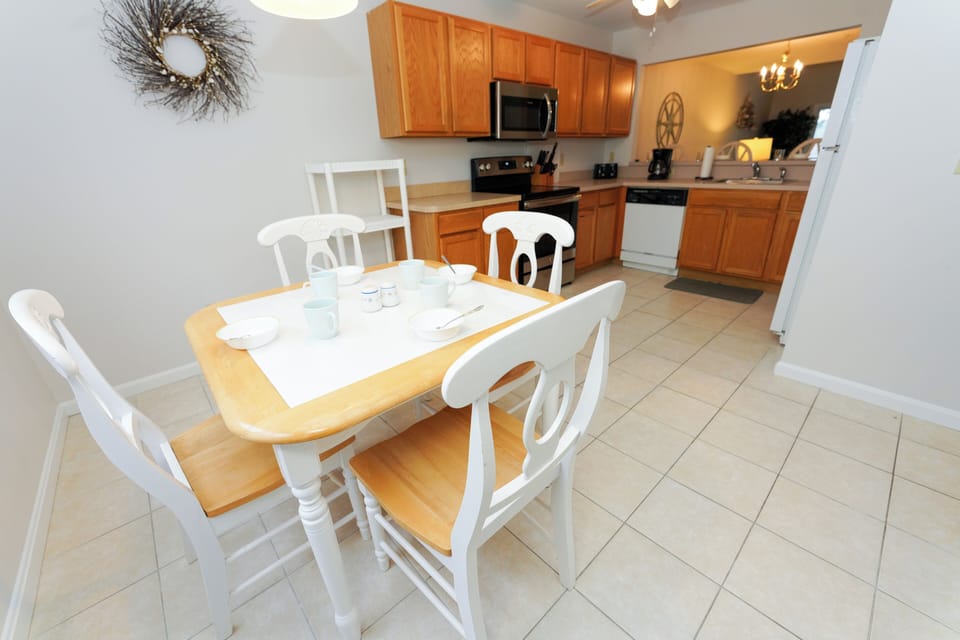 9405 Pettinaro Drive - Open Kitchen and Dining Area - View showing the open-concept dining space with a white-and-wood dining table adjacent to the kitchen, featuring traditional wooden cabinetry and light tile flooring.