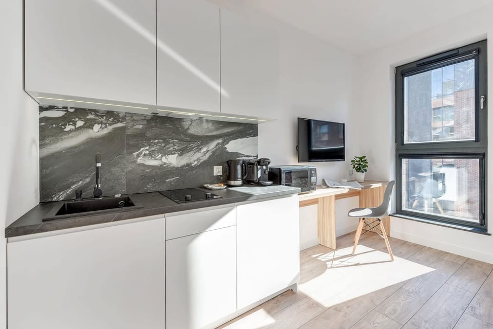 A contemporary kitchen with a black marble backsplash, white cabinetry, and essential appliances. Large windows ensure a bright cooking environment.