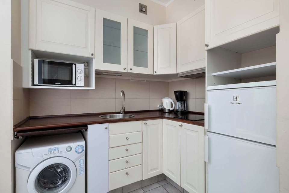 A similar kitchen interior shows white cabinetry and wooden-style countertops with built-in appliances. The sink and cooking area are neatly organized. The space appears clean and functional.