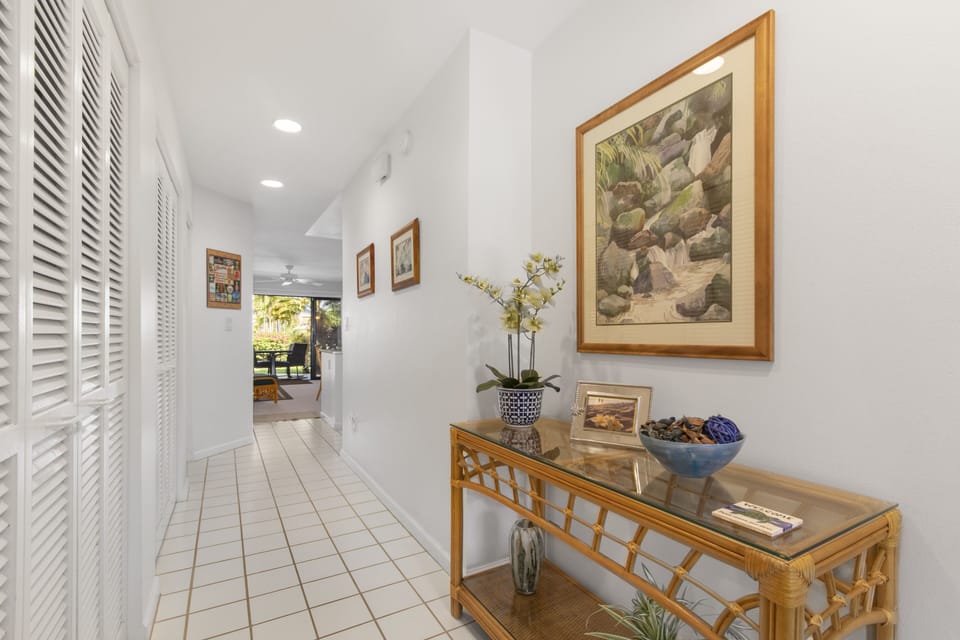 Step into a bright hallway adorned with tropical art and fresh orchids, leading you toward sunlit outdoor spaces that await your relaxation.