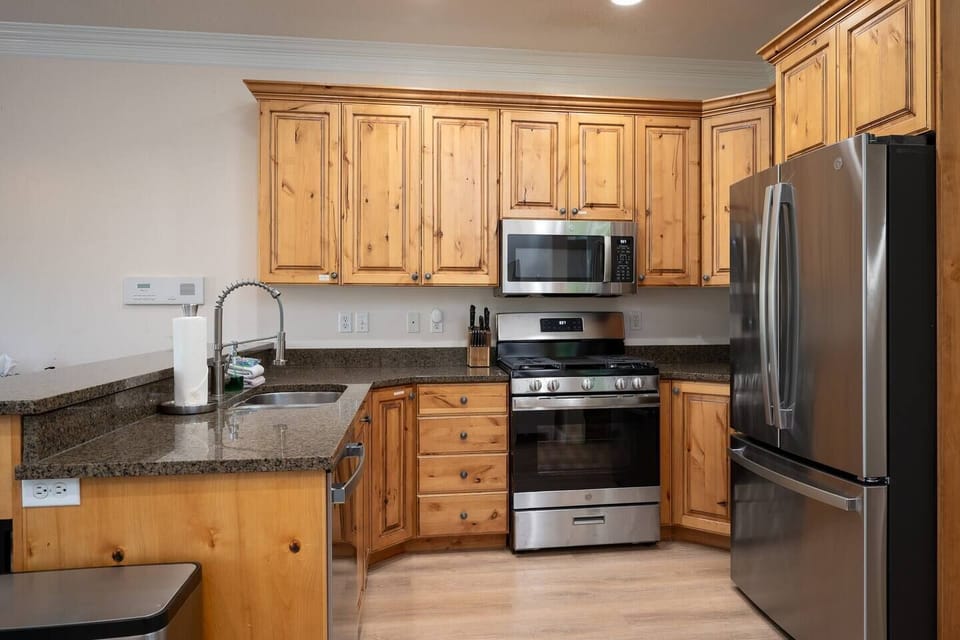 The gourmet kitchen features a breakfast bar with seating for three and is equipped with stainless steel appliances, including a microwave, gas stove, and spacious refrigerator.