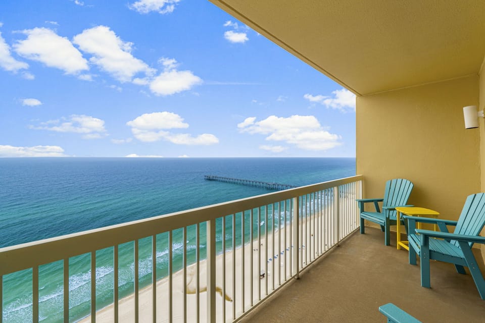 Balcony view with the Gulf pier visible in the distance, emerald water, and white sand stretching out below.