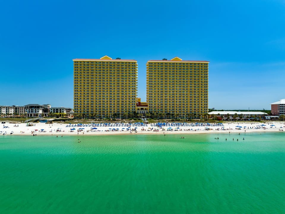 Calypso Resort and Towers from the Gulf, showing the twin towers rising directly above the private beach and emerald water.