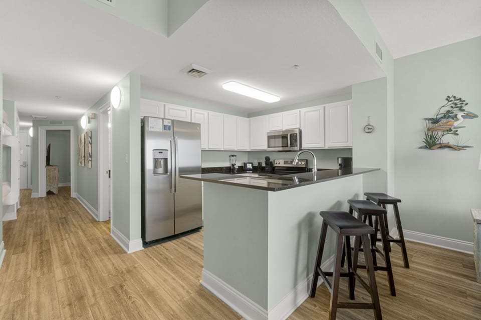 Fully equipped kitchen with stainless steel appliances, dark granite countertops, white cabinetry, and a breakfast bar with seating for three.