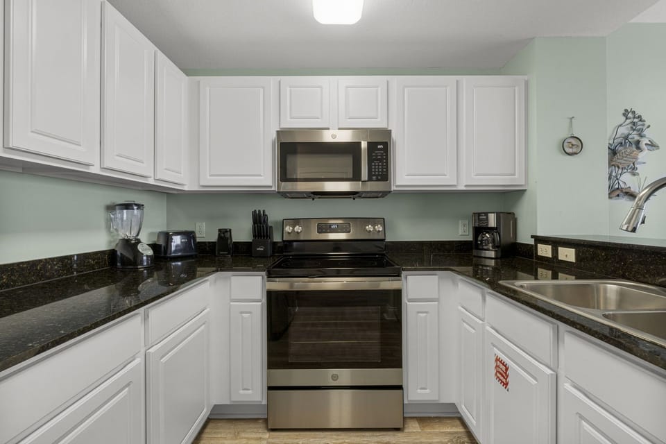 Well-stocked kitchen with stainless steel range and microwave, dark granite countertops, white cabinetry, and everything you need for cooking in.