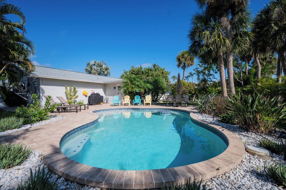 Your private tropical oasis awaits with a sparkling pool surrounded by swaying palms and colorful loungers under endless blue skies.