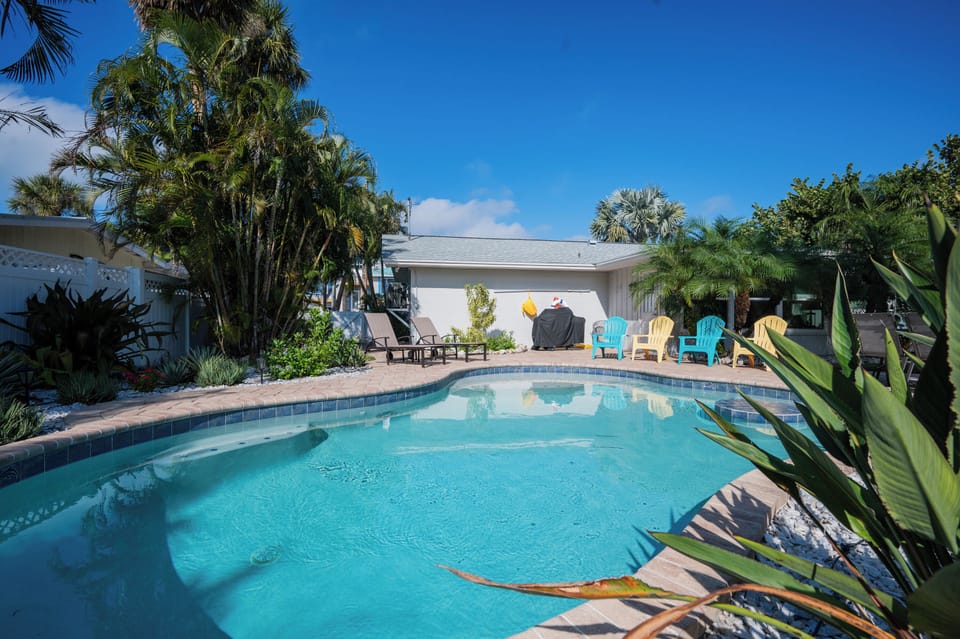 Your private tropical oasis awaits with crystal-clear pool waters surrounded by swaying palms and colorful poolside chairs for ultimate relaxation.