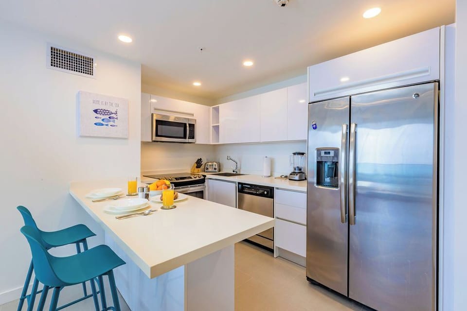 Your fully equipped kitchen awaits, featuring stainless steel appliances, sleek white cabinetry, and a breakfast bar for casual dining—perfect for preparing meals at home during your stay.