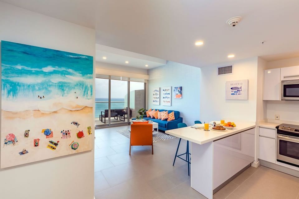 Sun-drenched open-concept living with coastal artwork, modern kitchen, and ocean-view terrace beckons you to unwind in airy, beachside luxury.