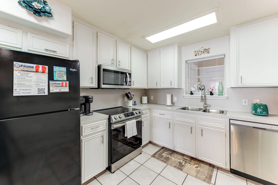 Your fully equipped kitchen features bright white cabinetry, stainless steel appliances, and natural light from the skylight above.