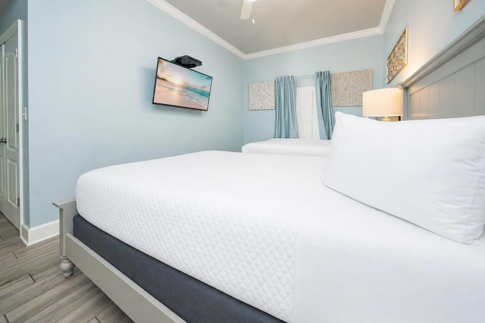 Relax in this serene guest bedroom featuring two queen beds, a TV, and soft blue decor for a restful stay