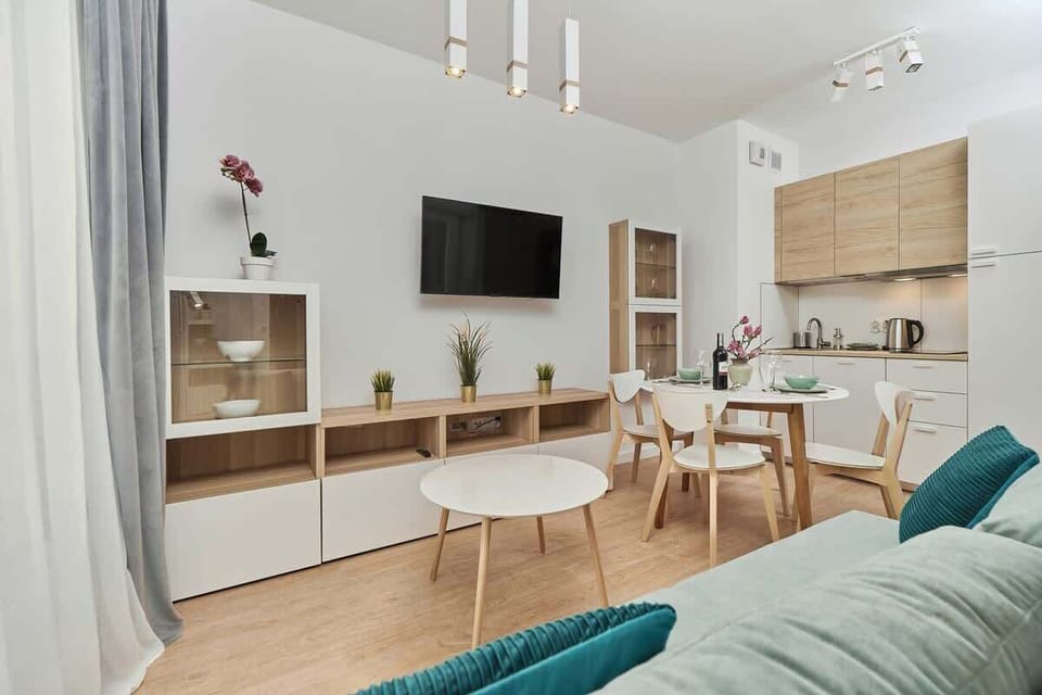 Another angle of the living room, showcasing a dining area with a wooden table and teal chairs. An open-plan design connects it to the kitchen.