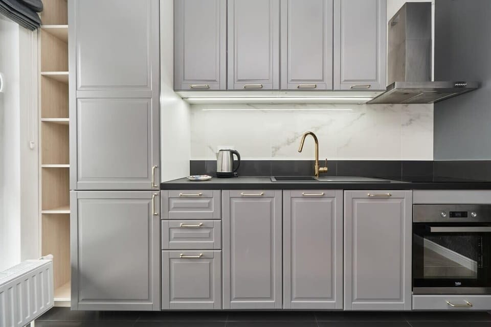 A contemporary kitchen with gray cabinetry, white countertops, and gold accents, including a sleek faucet. It includes modern appliances.