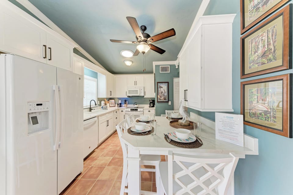 Your coastal kitchen awaits with crisp white cabinetry, modern appliances, and a cozy island perfect for morning coffee or evening conversations under the warm ceiling fan glow.