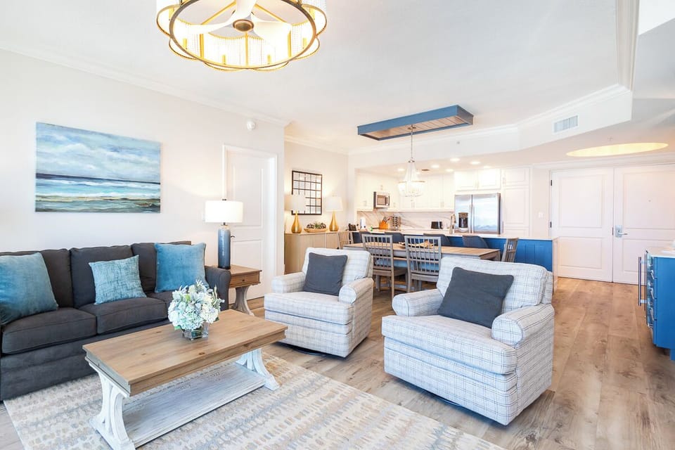 Relax in your open-concept living space featuring coastal blue accents, modern furnishings, and a fully equipped kitchen perfect for your seaside getaway.