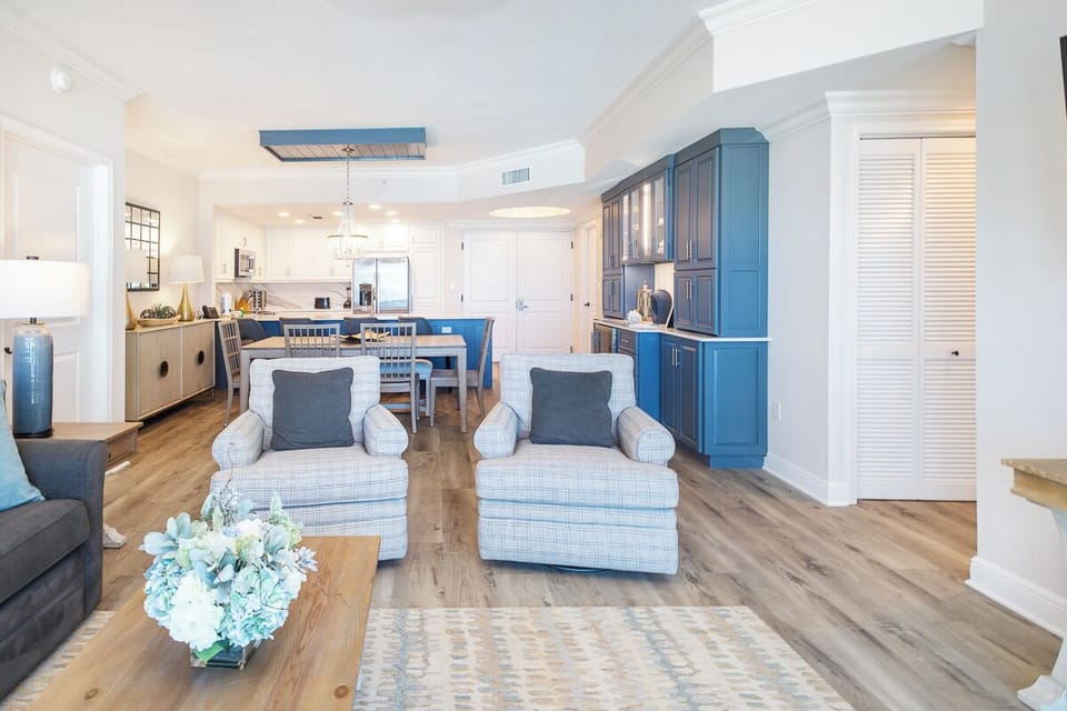 Relax in your open-concept living space with coastal blues, hardwood floors, and stylish furnishings flowing into a fully equipped kitchen.