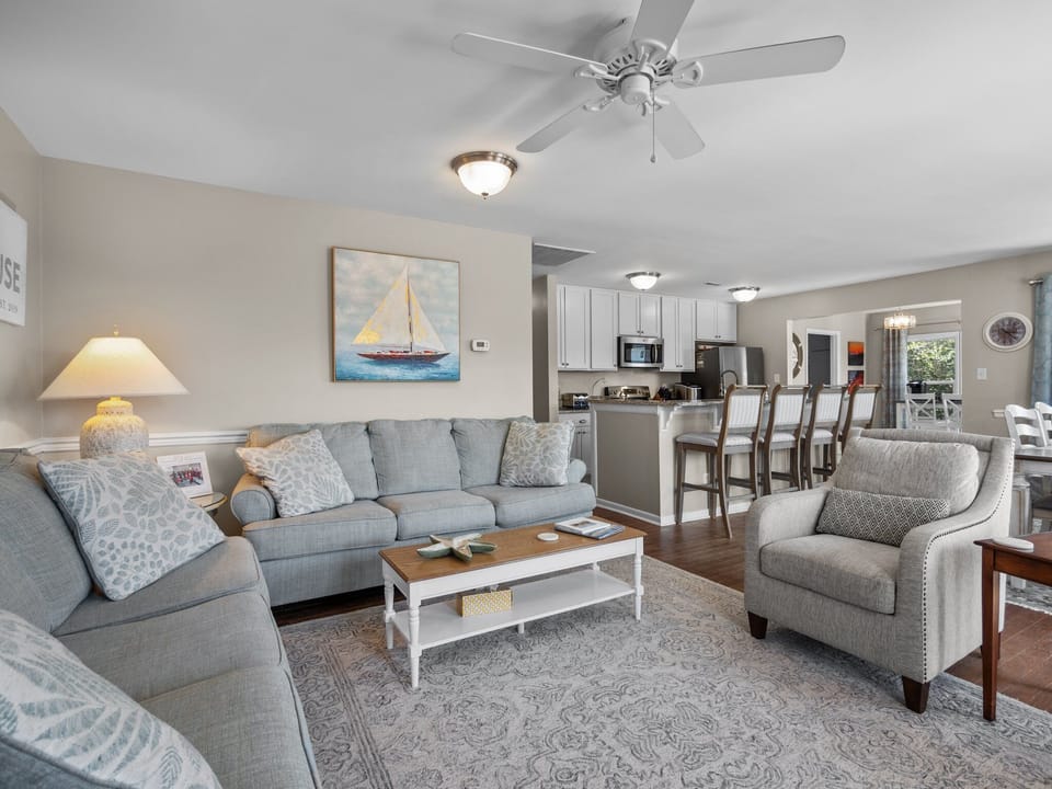 Relax in your elegant living space featuring plush seating, coastal artwork, and an open kitchen perfect for entertaining.