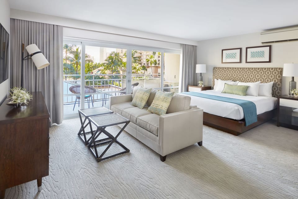 Your spacious suite blends rest and relaxation—sink into the plush king bed or lounge on the sofa, then step onto your private balcony with tropical views and waterside scenery.