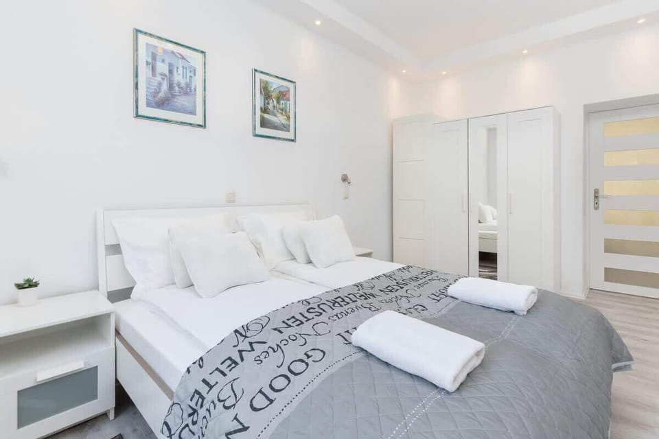 Bright, cosy bedroom with large bed with white linen and white large wardrobe.