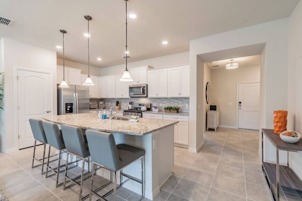 Step into a stylish kitchen where sleek, white cabinetry meets a stunning granite island, perfect for casual breakfasts or lively gatherings. The modern pendant lights above add a warm glow, enhancing the inviting atmosphere.