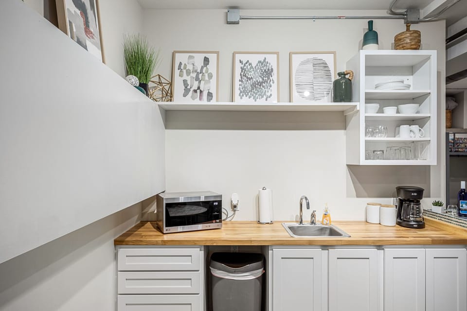 Compact kitchen setup w/ sink, microwave & open shelving to keep essentials within reach.