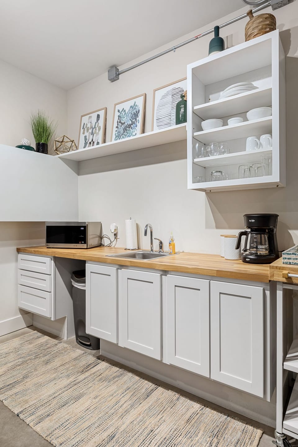 Clean kitchenette w/ wood countertops, coffee maker & essentials neatly organized.