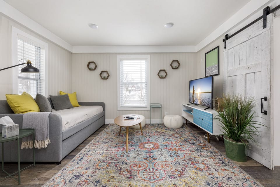 Bright living room w/ vaulted ceilings, plush sofa, colorful rug & wall-mounted TV for cozy movie nights.