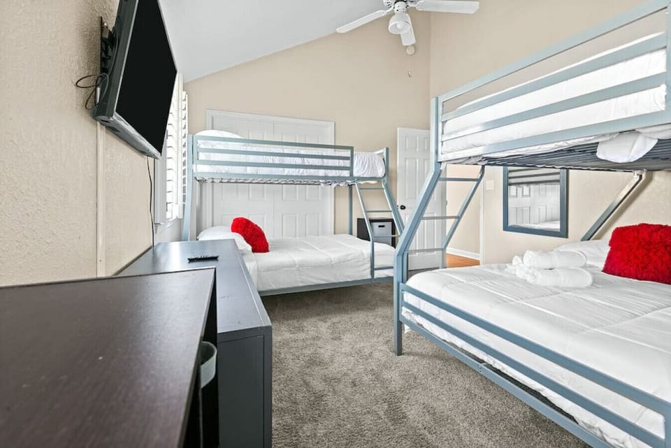 Reverse view of the bunk bedroom showing both gray bunk-bed setups, wall-mounted television, two dressers, closet doors, and vaulted ceiling.