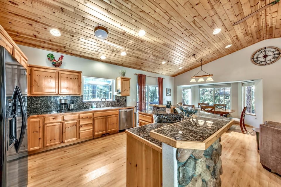 Cook memorable meals in your spacious kitchen featuring rustic wood cabinets, granite countertops, and modern appliances beneath warm knotty pine ceilings.