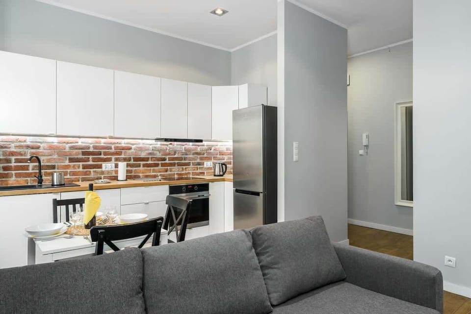 A bright living room with a gray sofa, a small round table, and a view into the kitchen area.