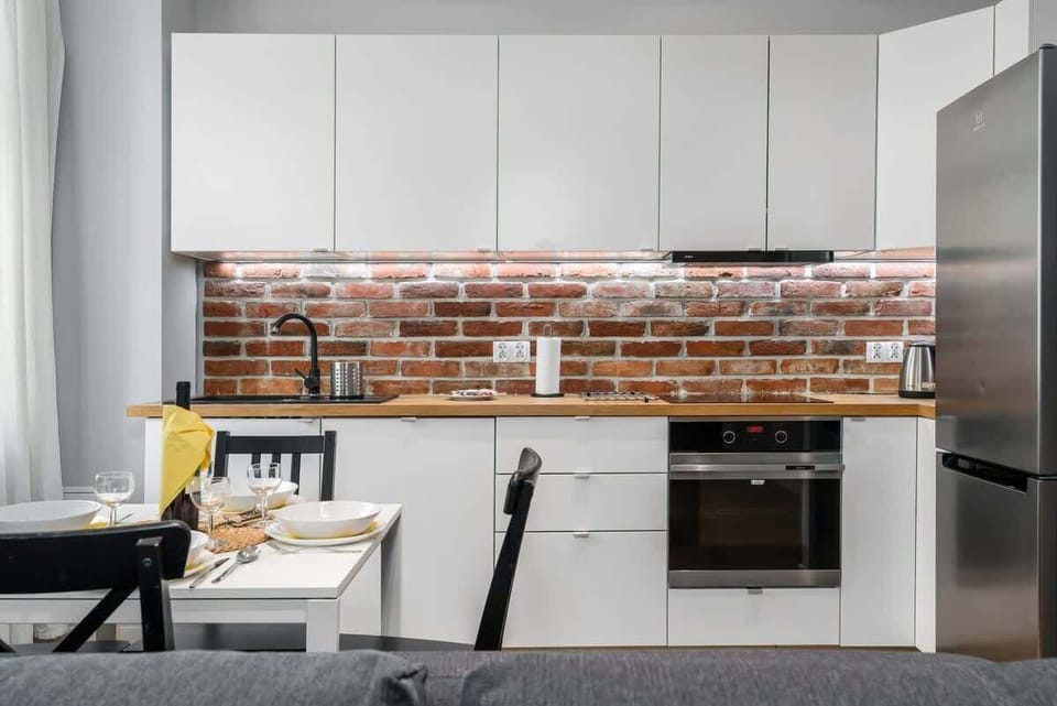 Close-up of a modern kitchen with exposed brick backsplash, stove, and cabinets.